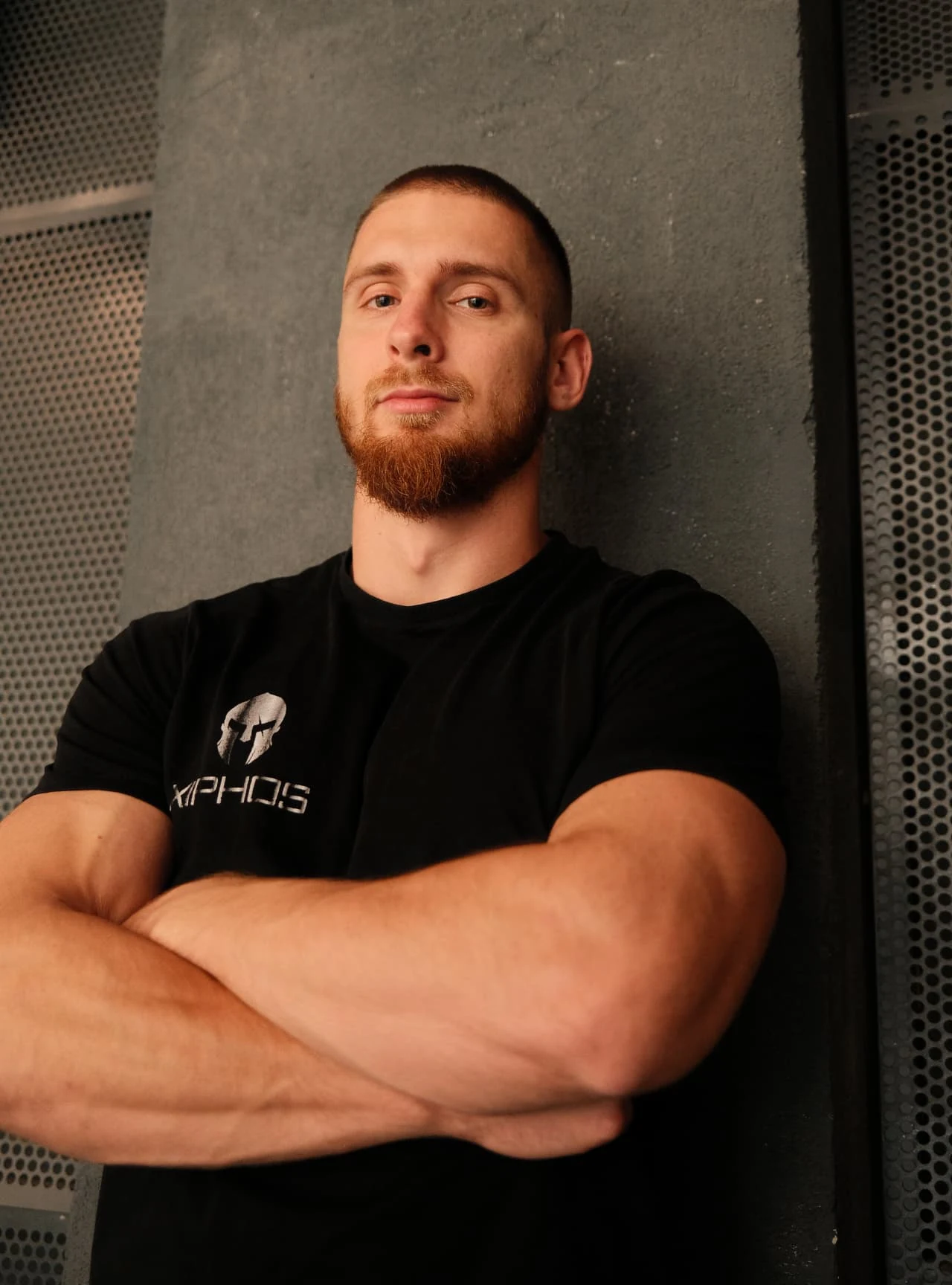 Luka standing with crossed arms against an industrial gym wall